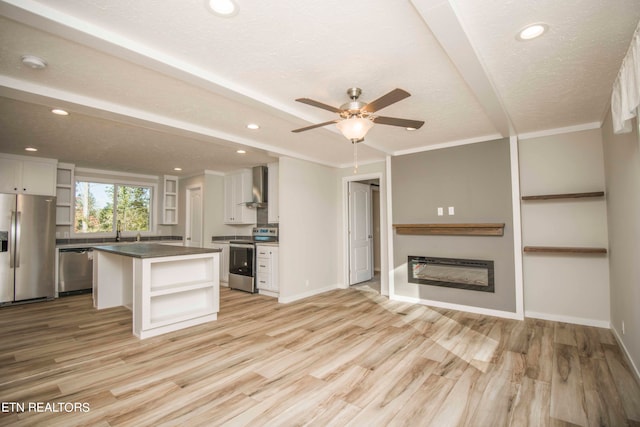 kitchen featuring white cabinets, a center island, wall chimney range hood, stainless steel appliances, and light hardwood / wood-style floors