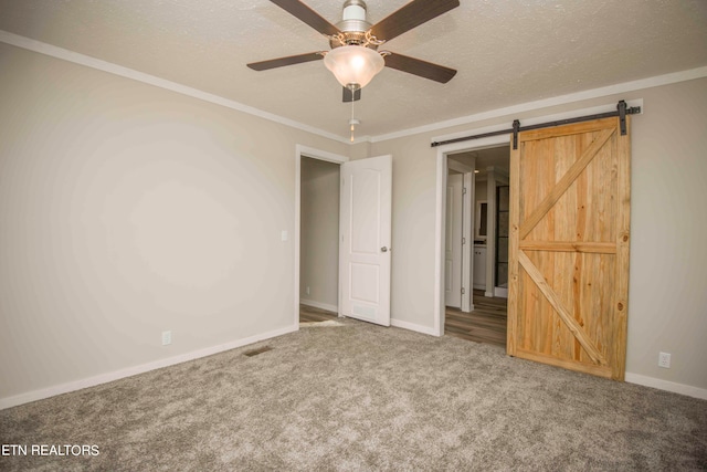 unfurnished bedroom with carpet, a textured ceiling, ceiling fan, crown molding, and a barn door