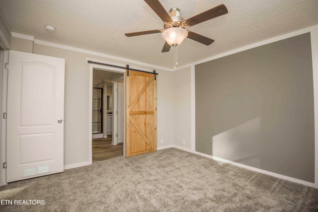 unfurnished bedroom featuring carpet, a textured ceiling, ornamental molding, ceiling fan, and a barn door