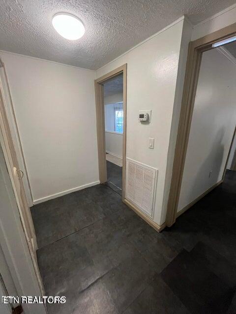 hall with a textured ceiling, visible vents, and baseboards