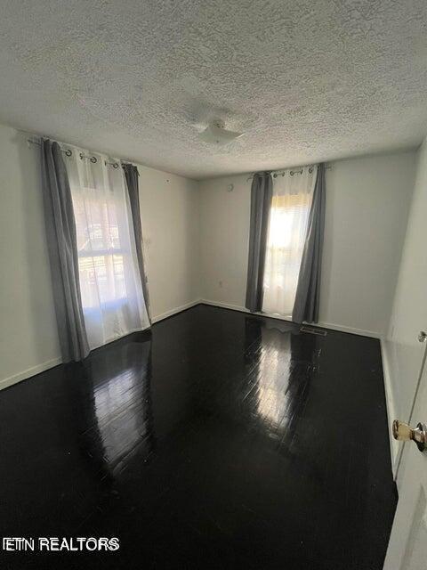 empty room featuring baseboards, a textured ceiling, and hardwood / wood-style floors