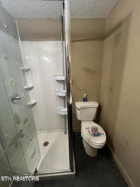 bathroom featuring toilet, a shower stall, baseboards, and a textured ceiling