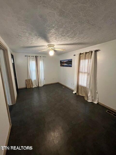 empty room featuring a ceiling fan, visible vents, baseboards, and a textured ceiling