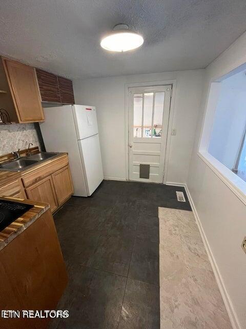 kitchen with baseboards, brown cabinetry, freestanding refrigerator, a textured ceiling, and a sink