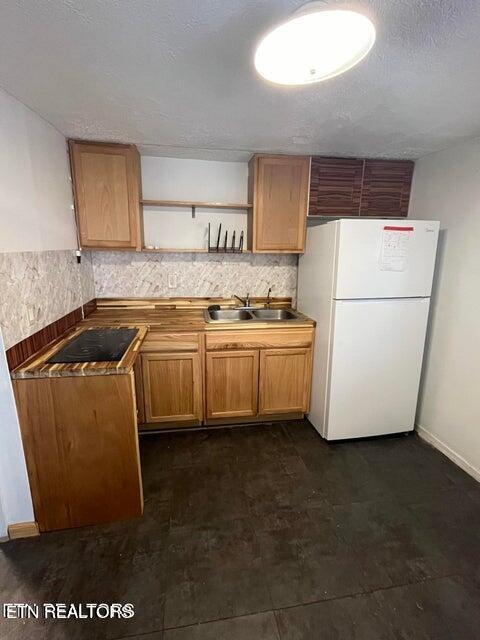 kitchen with freestanding refrigerator, a sink, black electric stovetop, open shelves, and backsplash