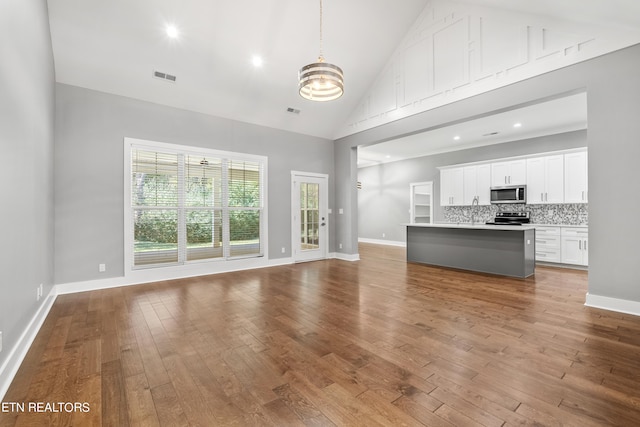 unfurnished living room with hardwood / wood-style flooring, high vaulted ceiling, sink, and a chandelier