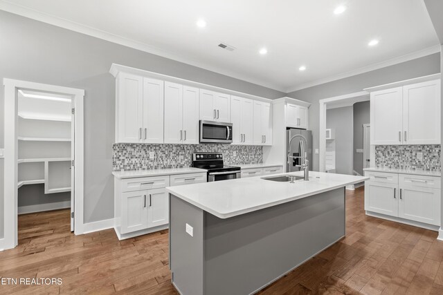 kitchen featuring appliances with stainless steel finishes, light hardwood / wood-style flooring, white cabinets, and a center island with sink