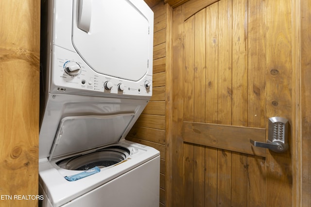 clothes washing area featuring wood walls and stacked washer and clothes dryer