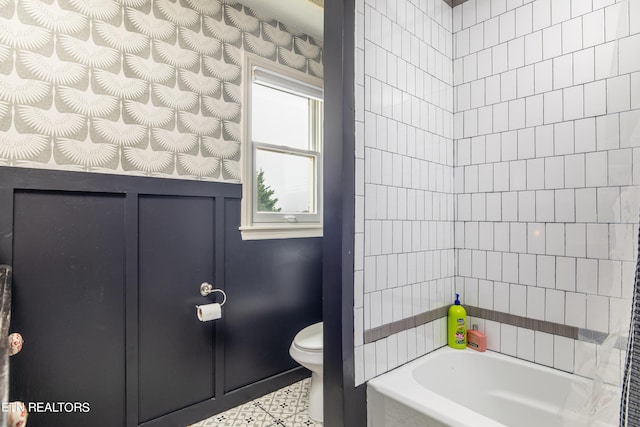 bathroom with a wainscoted wall, a washtub, and toilet