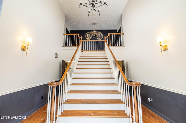 staircase featuring a chandelier, wainscoting, a textured ceiling, and wood finished floors