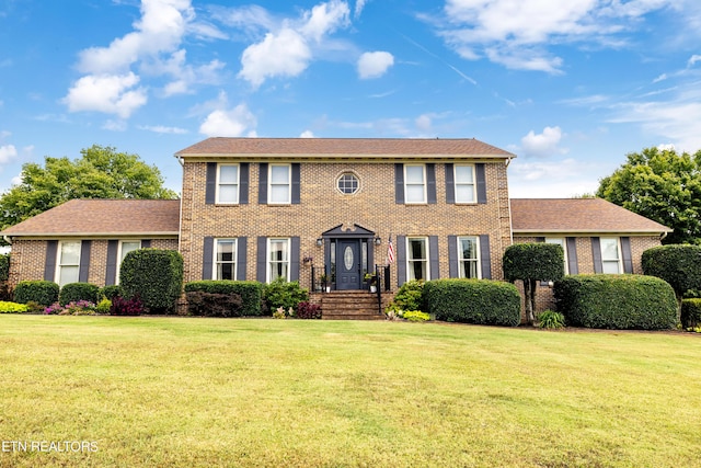 colonial house featuring brick siding, roof with shingles, and a front lawn