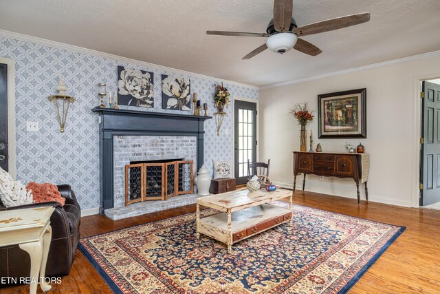 living room with crown molding, a textured ceiling, a brick fireplace, ceiling fan, and hardwood / wood-style flooring