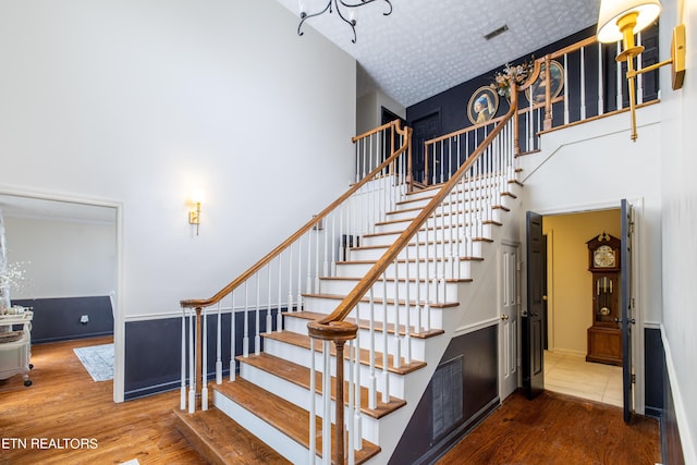 staircase featuring visible vents, a textured ceiling, a towering ceiling, and wood finished floors