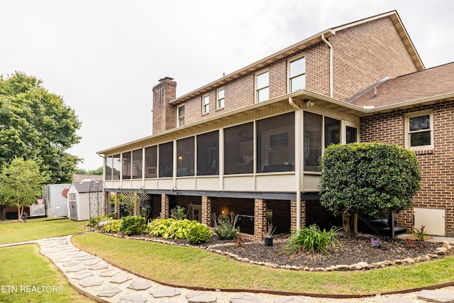 back of house featuring brick siding, a chimney, an outdoor structure, a sunroom, and a storage unit