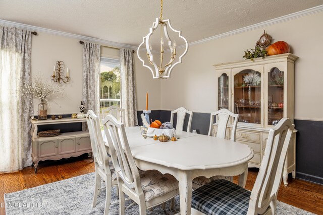 dining area with dark wood-type flooring, a chandelier, a textured ceiling, and ornamental molding