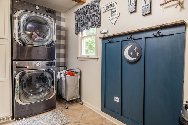 clothes washing area featuring stacked washing maching and dryer, cabinets, and tile patterned floors