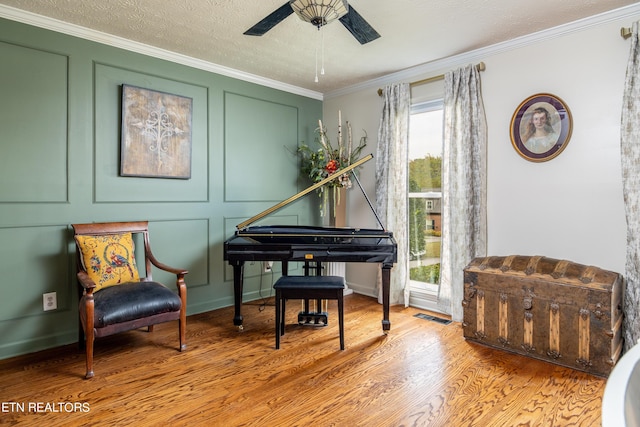 sitting room with visible vents, ornamental molding, wood finished floors, a decorative wall, and ceiling fan