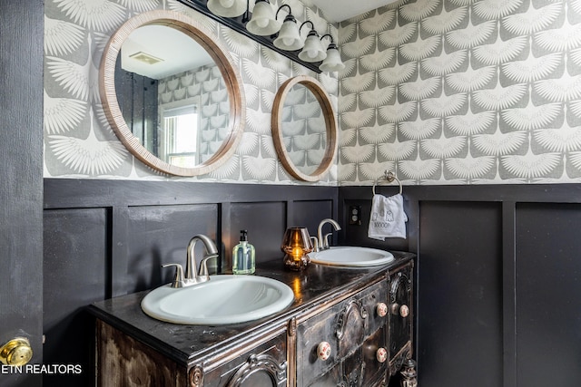 full bath featuring a sink, visible vents, double vanity, and a decorative wall