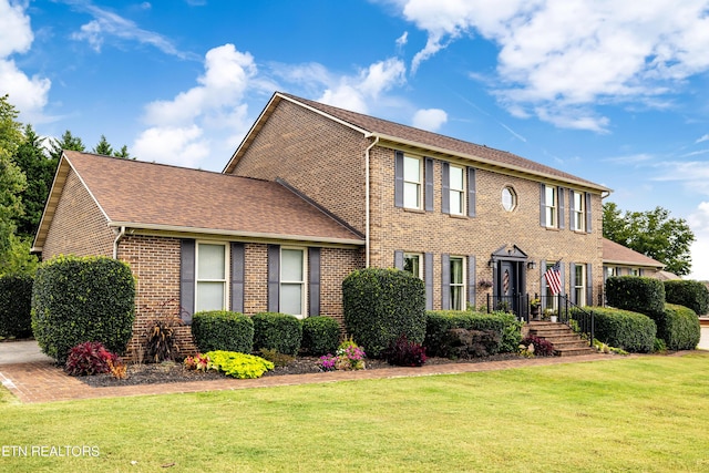 colonial home featuring brick siding, a shingled roof, and a front yard