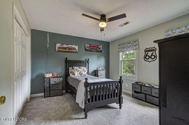 carpeted bedroom with a textured ceiling, ceiling fan, and a closet