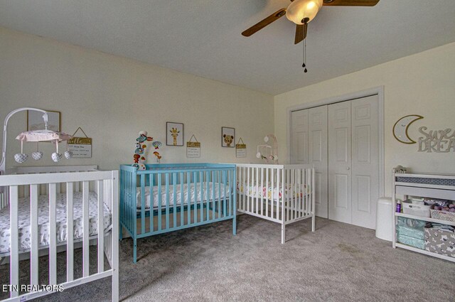 carpeted bedroom with a crib, ceiling fan, and a closet