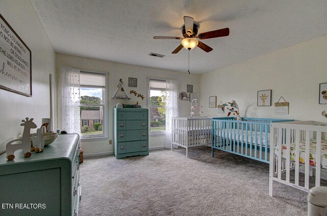 carpeted bedroom featuring ceiling fan, a nursery area, and a textured ceiling