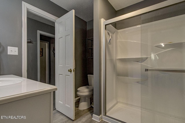 full bathroom featuring toilet, a textured ceiling, wood finished floors, a shower stall, and vanity