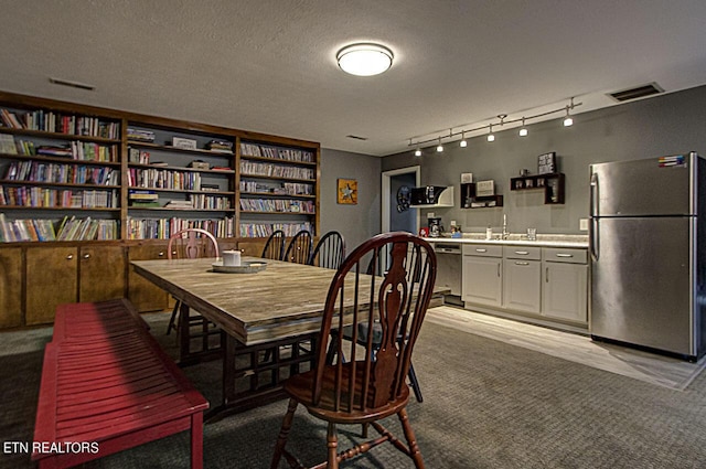 carpeted dining space with a sink, visible vents, a textured ceiling, and track lighting