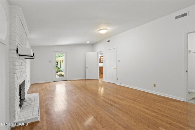 unfurnished living room featuring lofted ceiling, a brick fireplace, and light hardwood / wood-style floors