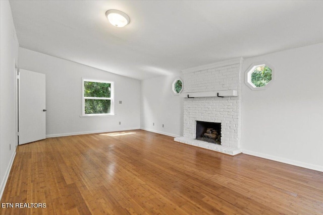 unfurnished living room with wood-type flooring, a brick fireplace, and vaulted ceiling