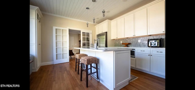 kitchen with appliances with stainless steel finishes, hanging light fixtures, an island with sink, white cabinets, and dark hardwood / wood-style flooring