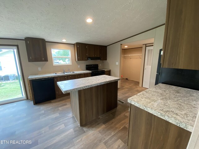 kitchen with a textured ceiling, black appliances, a center island, light hardwood / wood-style flooring, and sink