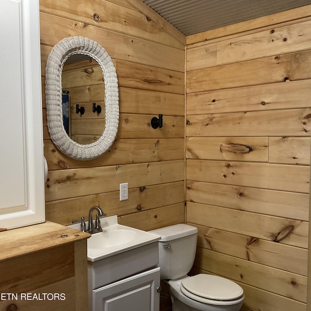 bathroom with toilet, vanity, and wooden walls