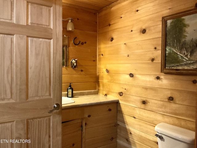 bathroom featuring toilet, wooden walls, and vanity