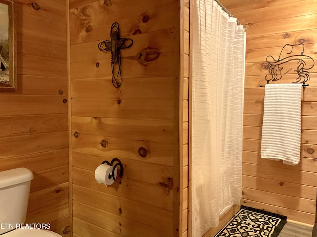 bathroom featuring toilet, wood walls, and a shower with shower curtain