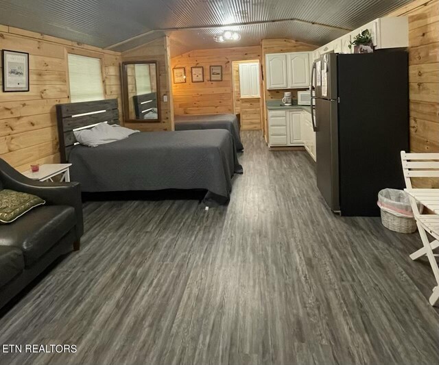 bedroom featuring vaulted ceiling, wood walls, dark wood finished floors, and freestanding refrigerator