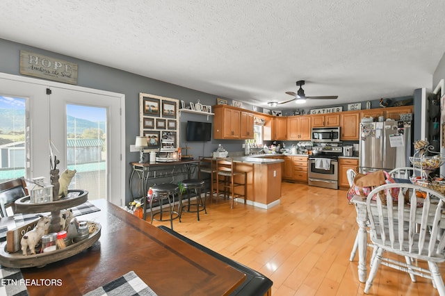 kitchen with appliances with stainless steel finishes, light hardwood / wood-style floors, kitchen peninsula, ceiling fan, and a breakfast bar