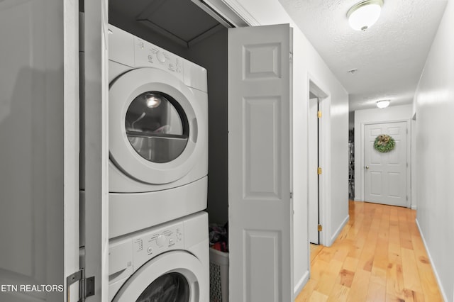 clothes washing area featuring stacked washer and dryer, a textured ceiling, and light hardwood / wood-style flooring