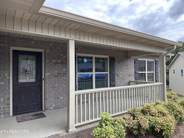 view of exterior entry featuring brick siding and covered porch