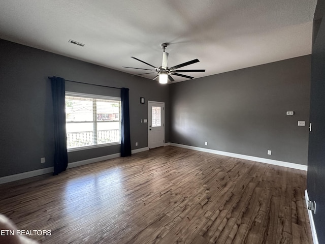 empty room with dark wood-type flooring, visible vents, baseboards, and ceiling fan