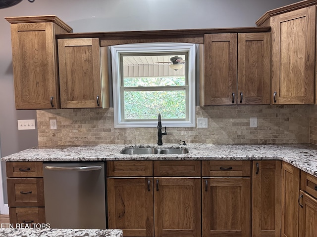 kitchen with brown cabinets, a sink, decorative backsplash, light stone countertops, and dishwasher