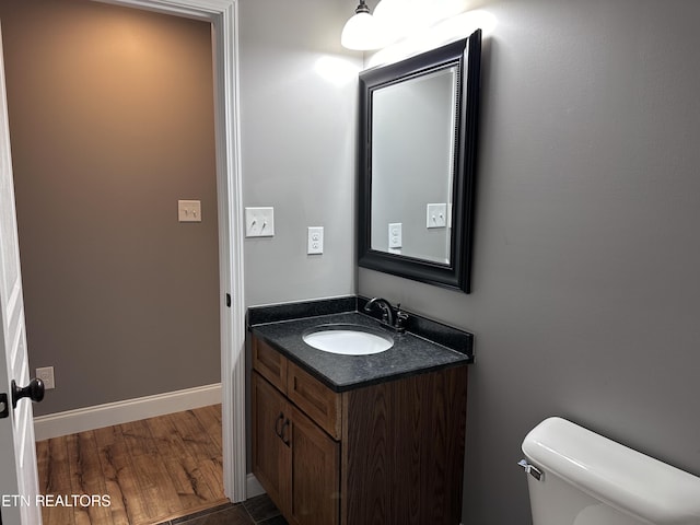 half bathroom featuring toilet, vanity, baseboards, and wood finished floors