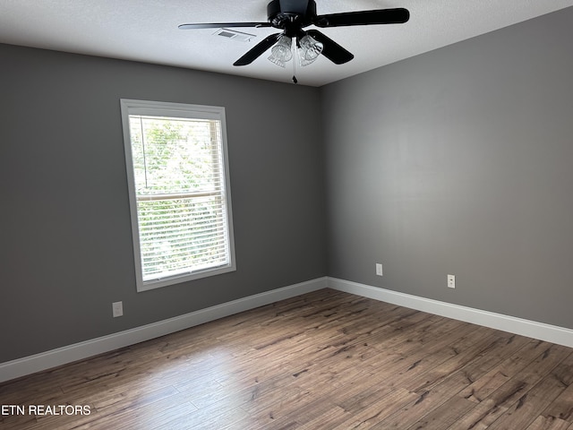 spare room with a textured ceiling, wood finished floors, visible vents, and baseboards