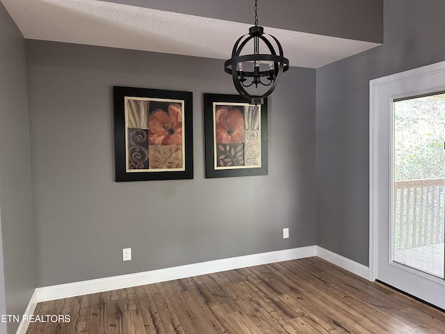 empty room with a chandelier, a textured ceiling, baseboards, and wood finished floors