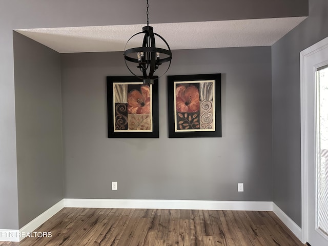 unfurnished dining area featuring dark wood-style floors, an inviting chandelier, a textured ceiling, and baseboards