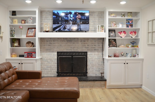 living room featuring built in features, crown molding, wood-type flooring, and a brick fireplace