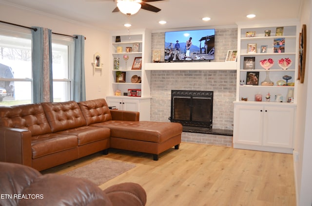 living room featuring a fireplace, light hardwood / wood-style flooring, built in shelves, crown molding, and ceiling fan