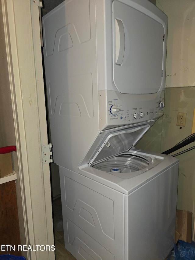 laundry area with dark wood-type flooring and stacked washer / dryer