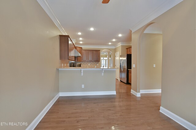 kitchen featuring a breakfast bar area, stainless steel refrigerator with ice dispenser, kitchen peninsula, ceiling fan, and light wood-type flooring