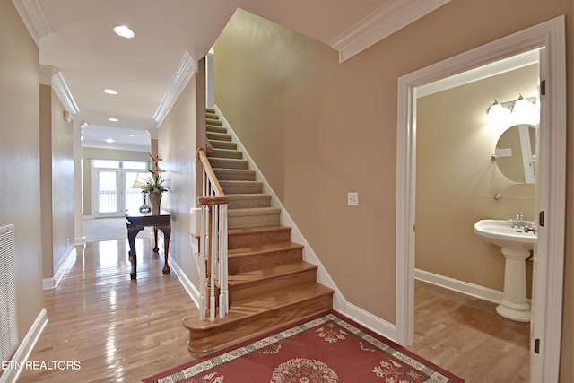 stairs featuring hardwood / wood-style floors, crown molding, and sink